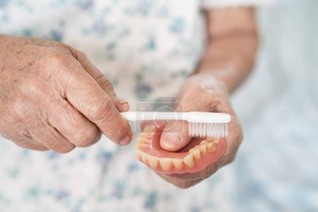 Asiatique femme âgée patient utiliser une brosse à dents pour nettoyer une prothèse partielle de dents de remplacement.