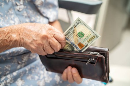 Photo for Asian senior woman holding and counting US dollar banknotes money in purse. Poverty, saving problem in retirement. - Royalty Free Image