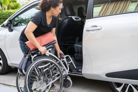 Asiatische behinderte Frau im Rollstuhl steigt in ihr Auto, Barrierefreiheitskonzept.