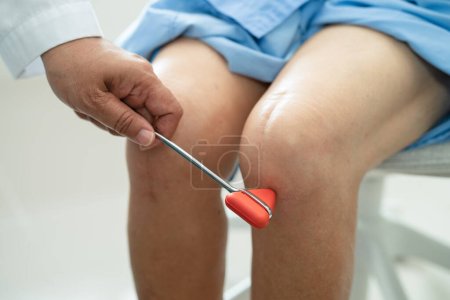 Foto de Médico asiático uso martillo golpe mujer mayor paciente para comprobar reflejo de rodilla, nervio y músculo en el hospital. - Imagen libre de derechos