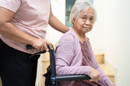 Pfleger helfen asiatischer oder älterer Frau, die im Rollstuhl sitzt, die Treppe im Haus hinauf.