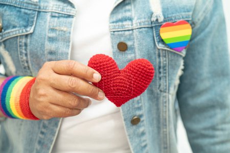 Asiatische Dame trägt Regenbogenfahne Armbänder und hält rotes Herz, Symbol des LGBT-Stolzes Monat feiern jährlich im Juni soziale Schwule, Lesben, Bisexuelle, Transgender, Menschenrechte.
