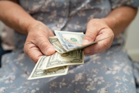 Femme âgée asiatique tenant et comptant l'argent des billets en dollars américains dans le sac à main. Pauvreté, problème d'épargne à la retraite.