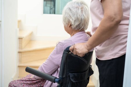 Caregiver help asian or elderly old woman sitting wheelchair support up the stairs in home.