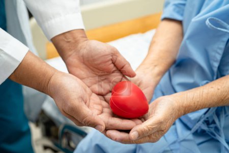 Photo for Doctor give red heart to Asian elderly woman patient in her hand on bed in hospital. - Royalty Free Image