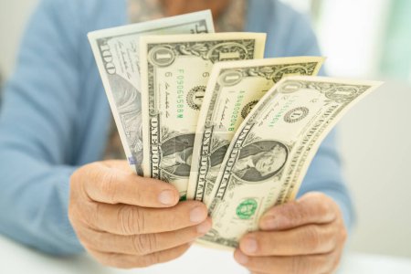 Mujer mayor asiática sosteniendo y contando billetes en dólares estadounidenses dinero en el bolso. Pobreza, problema de ahorro en la jubilación.