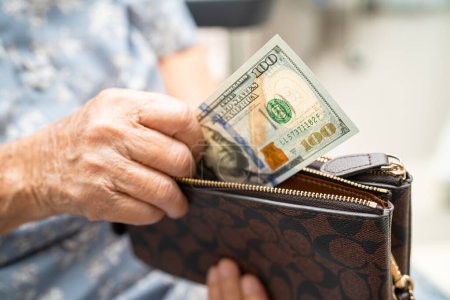 Asiatische Seniorin hält und zählt US-Dollar-Banknoten in der Handtasche. Armut, Sparproblem im Ruhestand.