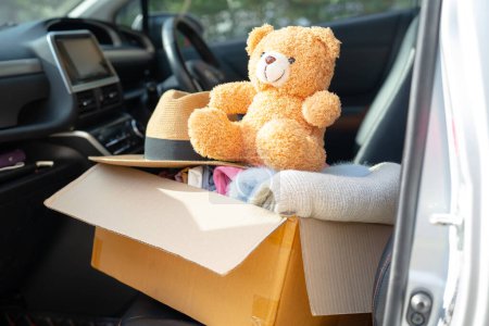 Volunteer provide clothing donation box with used clothes and doll in car to support help for refugee, homeless or poor people in the world.