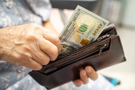 Femme âgée asiatique tenant et comptant l'argent des billets en dollars américains dans le sac à main. Pauvreté, problème d'épargne à la retraite.