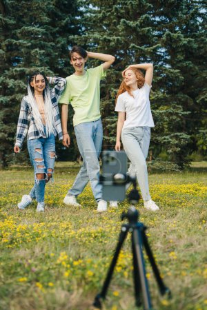 Téléchargez les photos : Portrait de trois adolescents de la génération Z filmant des vidéos pour les médias sociaux dans le parc d'été. Enregistrement d'une bobine pour un site de médias sociaux. Belle pour la conception de style de vie. - en image libre de droit