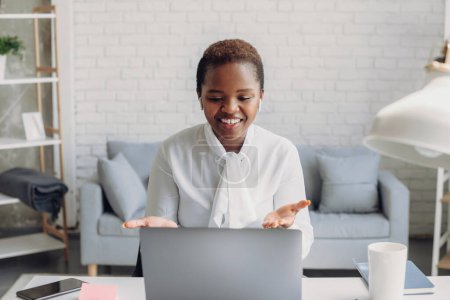 Happy beautiful african american woman freelancer, talking by video call having an online meeting with colleagues. Female having online web conference at home