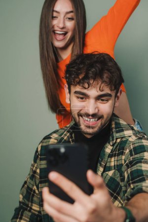 Foto de Young woman enjoying dancing with one hand up, man using phone isolated on gray background. Recording a video. - Imagen libre de derechos