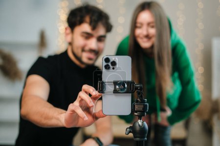 Photo for Smiling young couple with happy faces looking at phone camera, bloggers recording videoblog at home. Video live streaming. - Royalty Free Image