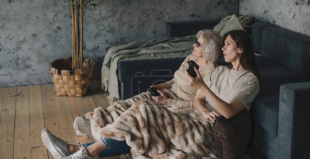 Photo for Competition of a mother and daughter playing video games indoors at home, sitting on cozy floor and enjoying themselves. They have great and fun time. Happy - Royalty Free Image