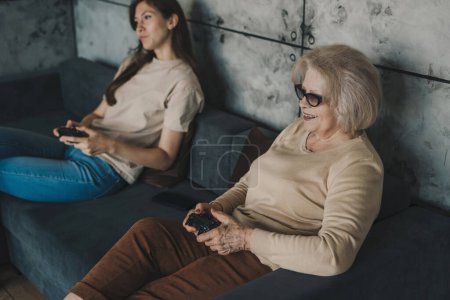 Photo for Pretty millennial women relaxing at home, resting on sofa playing video games together in a living room at home. Laughing family with happiness. - Royalty Free Image