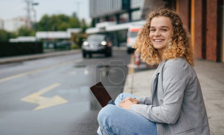 Photo for Smiling caucasian student girl sitting on street working on laptop, preparing for exams outdoors. Technology, education and remote working concept. Online - Royalty Free Image