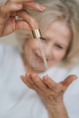 Photo for Closeup cut portrait of senior womans hands putting drop of antiaging pipette serum essence oil on finger hand. Anti wrinkle prevention skin care products - Royalty Free Image