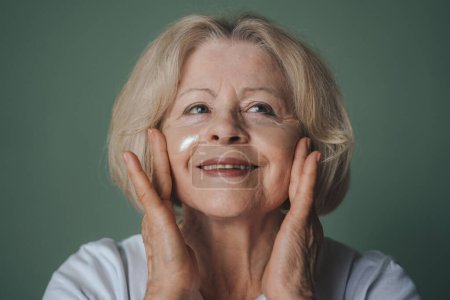 Photo for Front view portrait of a positive joyful woman applying eye patches on her face while wanting to have fresh skin. Beautiful for lifestyle design. Skin care - Royalty Free Image