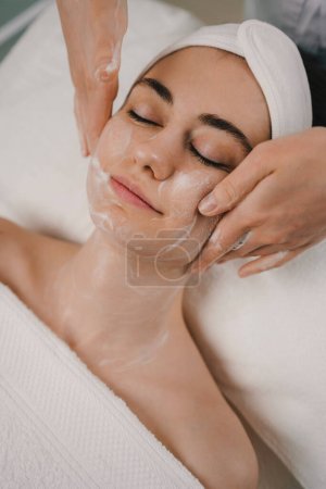 Téléchargez les photos : Vue rapprochée d'une belle femme allongée sur le lit tout en ayant son traitement de nettoyage du visage avec de la mousse. Massage corporel. Traitement thérapeutique, peau de beauté - en image libre de droit