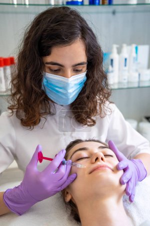 Beautician injecting hyaluronic acid into the lips of a girl with a syringe. The cosmetologist doctor performing the procedure in the cosmetology office