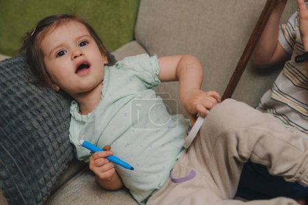 Porträt eines kleinen kaukasischen Mädchens, das mit blauem Filzstift auf dem Sofa liegt. Kindheit Freizeit Spaß Spiel Lernentwicklungskonzept