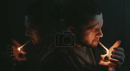 Photo for Handsome bearded man smoking cigarette sitting in the dark room. Hipster with lighter and cigarette. Closeup. - Royalty Free Image