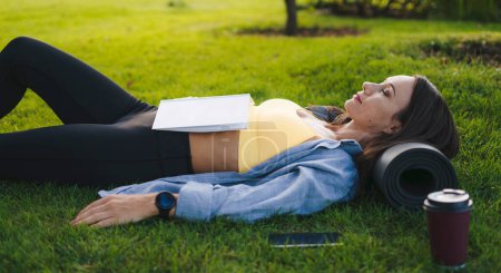 Foto de Mujer en el parque con libro para relajarse. Descanso, lectura y estudiante universitario en la hierba en el jardín del campus para la investigación, la narración de historias y la paz en el campo. - Imagen libre de derechos
