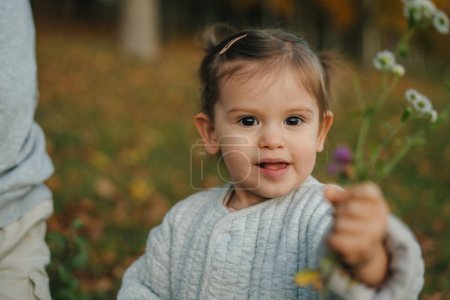 Happy little girl picking wild flowers in the meadow. Autumn seasonal outdoor activities for kids. Child explores nature.