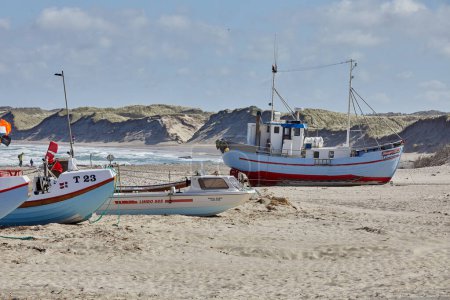Photo for Fishing boats in bright blue, white and red colors laying on the beach.In the background you kan see land and sand dunes. The sun is shining and the sky is blue. - Royalty Free Image