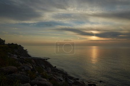 Photo for Sunset by the sea and beach. In the foreground there is grass and som big rocks. - Royalty Free Image