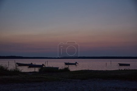 Photo for Dinghies on the water at dusk . In the foreground there is beach.The sky and water is pastel colored in blue and rosa. Vertikal. - Royalty Free Image