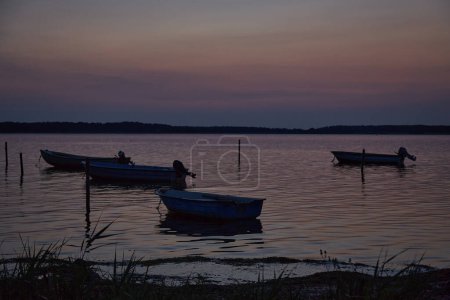 Photo for Dinghies on the water at dusk . In the foreground there is one dinghy and the two others are in the background.The sky and water is pastel colored in blue and rosa. Vertikal. - Royalty Free Image