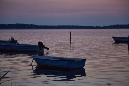 Photo for Dinghies on the water in at dusk.In the foreground there is one Dinghy and in the background there are two others.In horizon there is land and a lot of trees. The sky and the water is Patel colored in blue and rosa. - Royalty Free Image