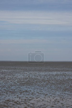 Photo for The mudflats by ebb. The bottom of the sea is visible and there is small puddles of water on the sand. he sky is blue with small white clouds. - Royalty Free Image