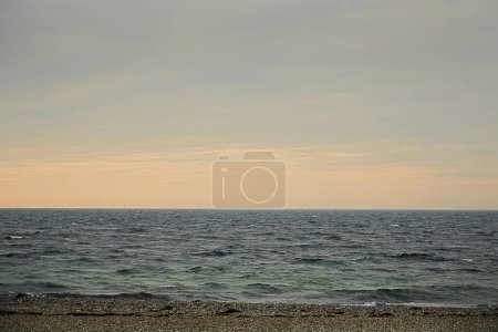 Photo for The sea with sand beach in front in the horizon the sky is yellow and blue. The sea is almost calm. - Royalty Free Image