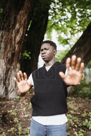 Photo for Shocked young 20s African man wear casual streetwear in park outdoor, doing stop not me sign with palms of hands. Denial gesture and face expression. Fall or spring season - Royalty Free Image