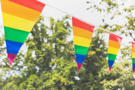 Colorful LGBTQ pride flags waving on sunny day with trees in background
