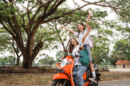 Photo for Two naughty high school girls ride on a reckless motorbike while celebrating graduation on the street - Royalty Free Image