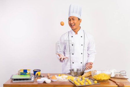 Téléchargez les photos : Male chef throwing eggs while making dough on the kitchen table on isolated background - en image libre de droit
