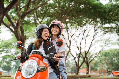 Téléchargez les photos : Deux étudiantes portant des casques et des vestes bavardant en moto ensemble - en image libre de droit