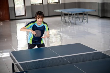 Photo for Female pingpong athlete holding ball and paddle preparing to serve at pingpong table - Royalty Free Image