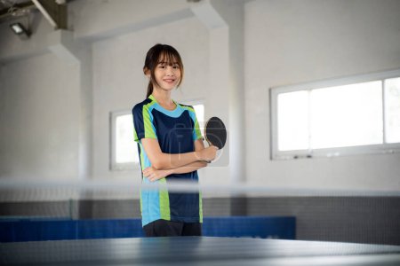 Photo for Female ping pong player smiling while holding paddle with arms crossed in indoor building - Royalty Free Image