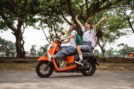 Photo for Two naughty high school girls riding motorbikes waving hands on the road - Royalty Free Image