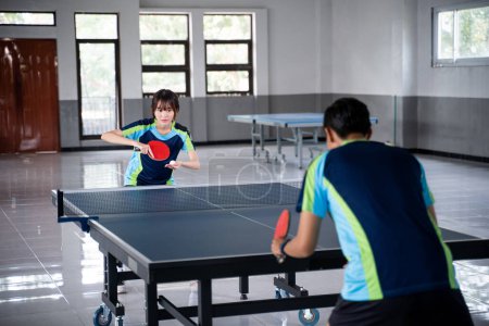 Photo for Asian female athlete preparing to serve against male athlete at ping pong table - Royalty Free Image