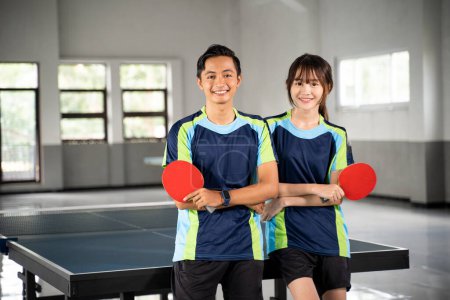 Photo for Two smiling asian athletes holding paddles while standing in front of a ping pong table - Royalty Free Image