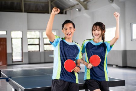 Photo for Two ping pong players holding paddles with raised fists near ping pong table - Royalty Free Image