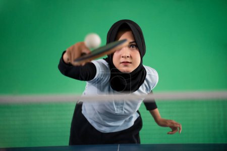 Photo for Asian Muslim female athlete hits the ball back while playing ping pong - Royalty Free Image