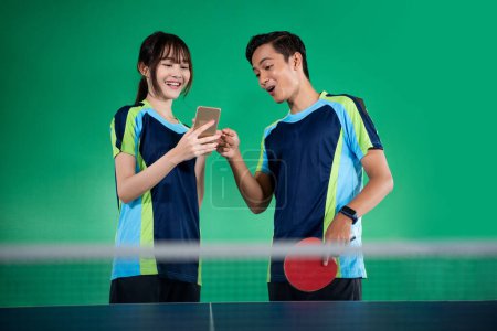 Photo for Female athlete using cellphone with her partner during a ping pong match - Royalty Free Image