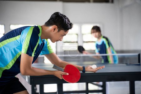 Photo for Male athlete carrying a ball and paddle while serving a ping pong game at a ping pong table - Royalty Free Image