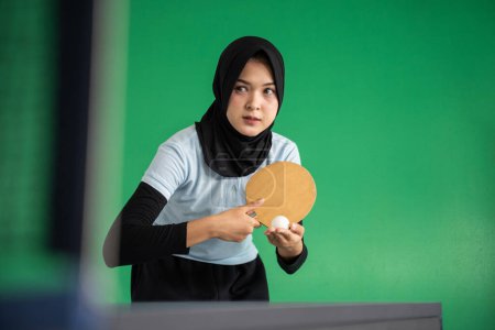 Photo for Muslim female table tennis player holding ball preparing to serve on green background - Royalty Free Image